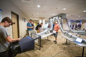Group of students closely examining a large machine in the TAB workshop.