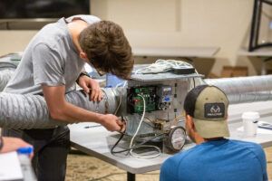 Two students working with an equipment setup, inspecting its components and wiring.